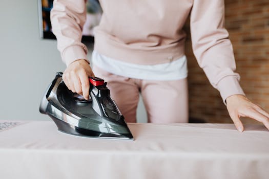 An adult ironing clothes on a board indoors, focusing on housework and fabric care.
